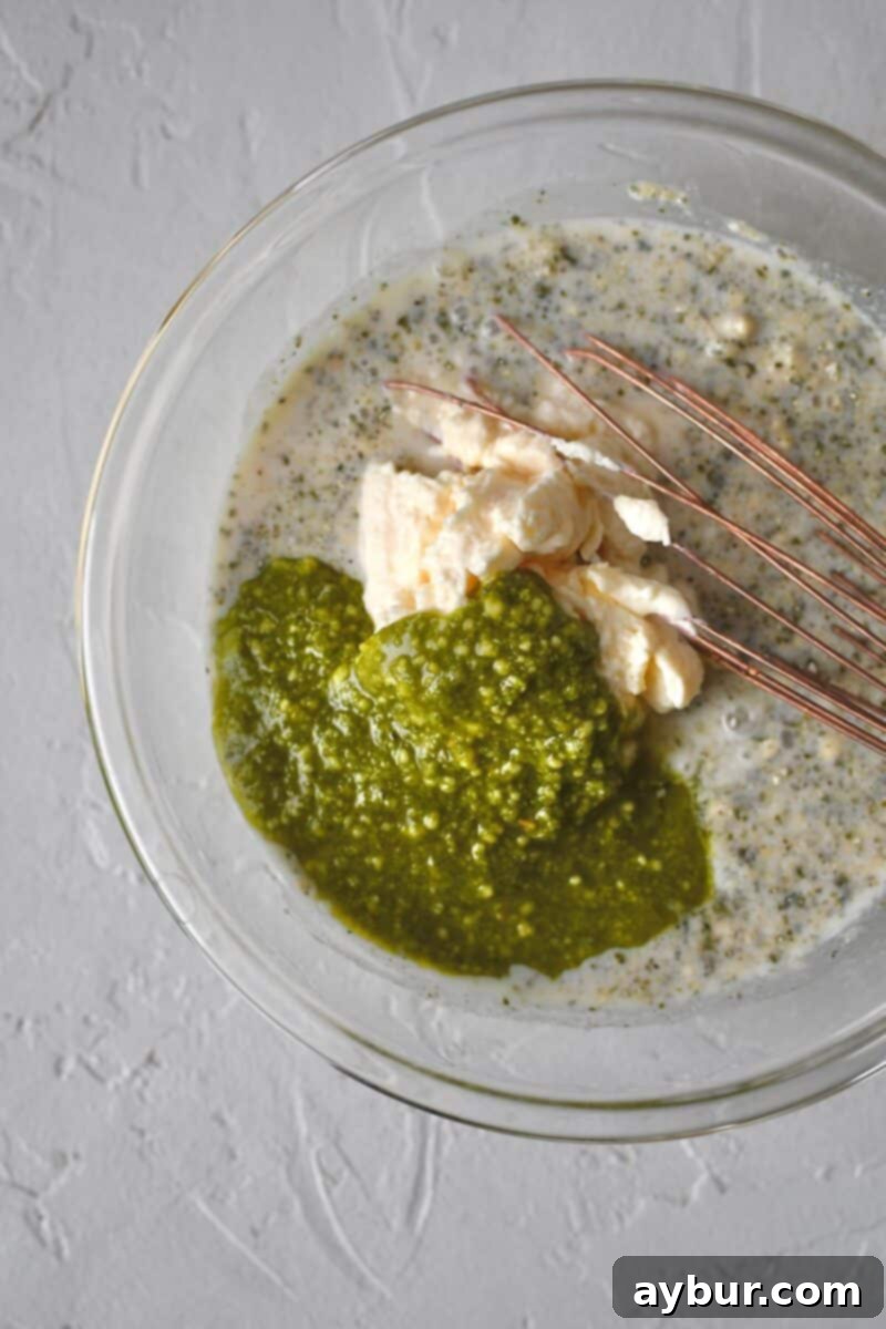 Adding mayonnaise and pesto to the ranch base in a bowl to create the creamy pesto ranch dressing.