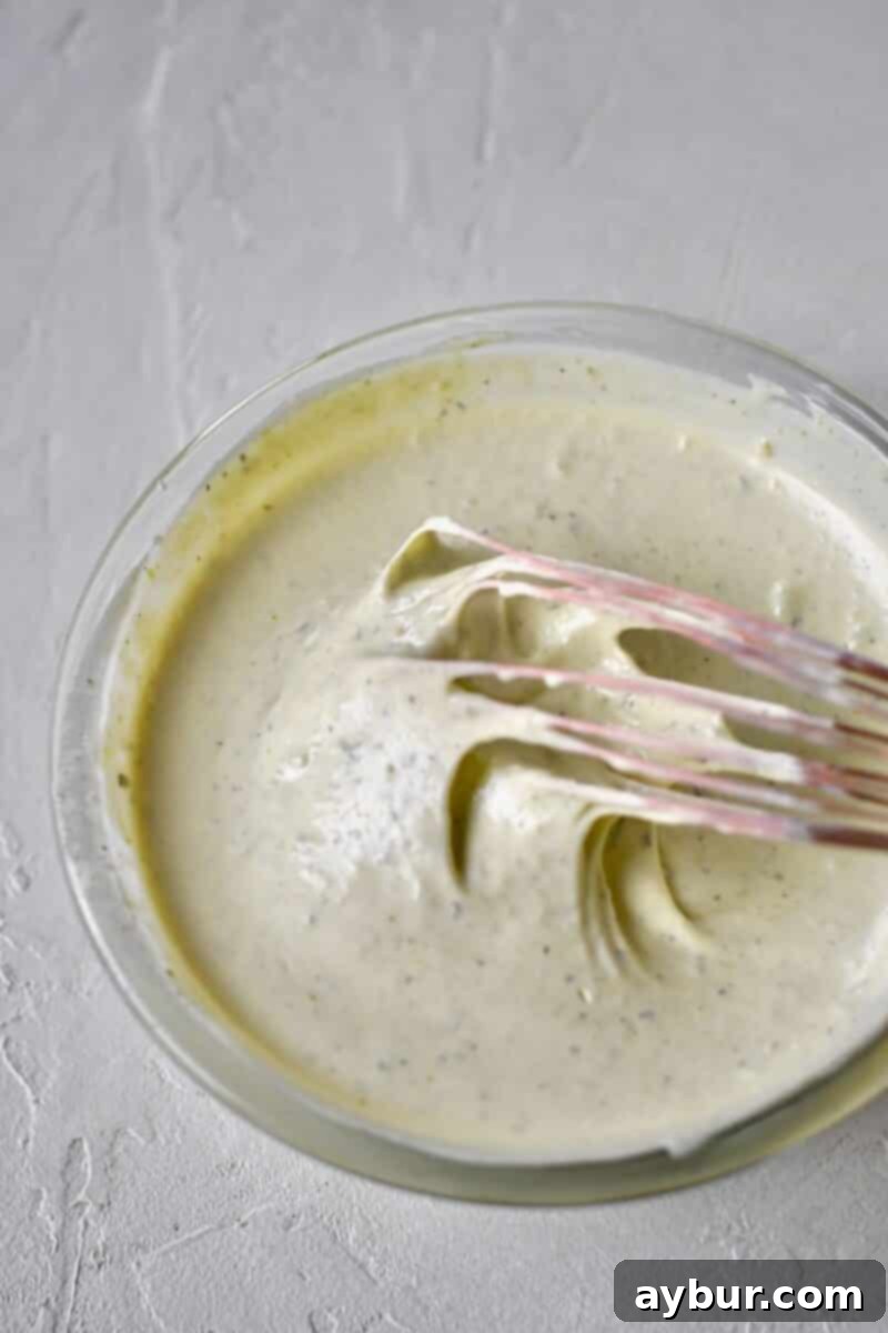 Vigorously whipping up the homemade pesto ranch dressing until smooth and combined.