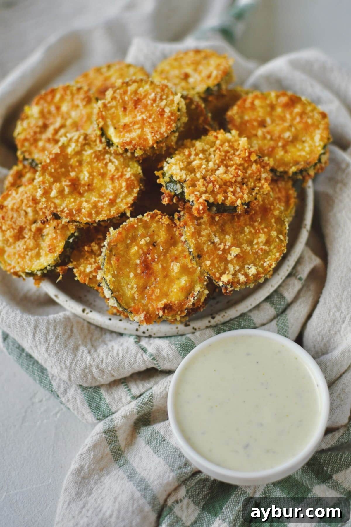 Baked Zucchini Crisps 12 A generous serving of crispy Zucchini Chips, artfully stacked on a plate, ready to be enjoyed as a delicious and healthy snack or side with a dip.