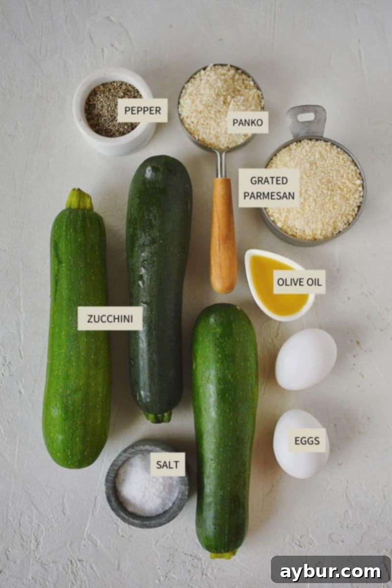 Baked Zucchini Crisps 3 A collection of fresh ingredients laid out on a counter, including whole zucchini, eggs, panko breadcrumbs, olive oil, and a wedge of Parmesan cheese, ready for making Zucchini Chips.