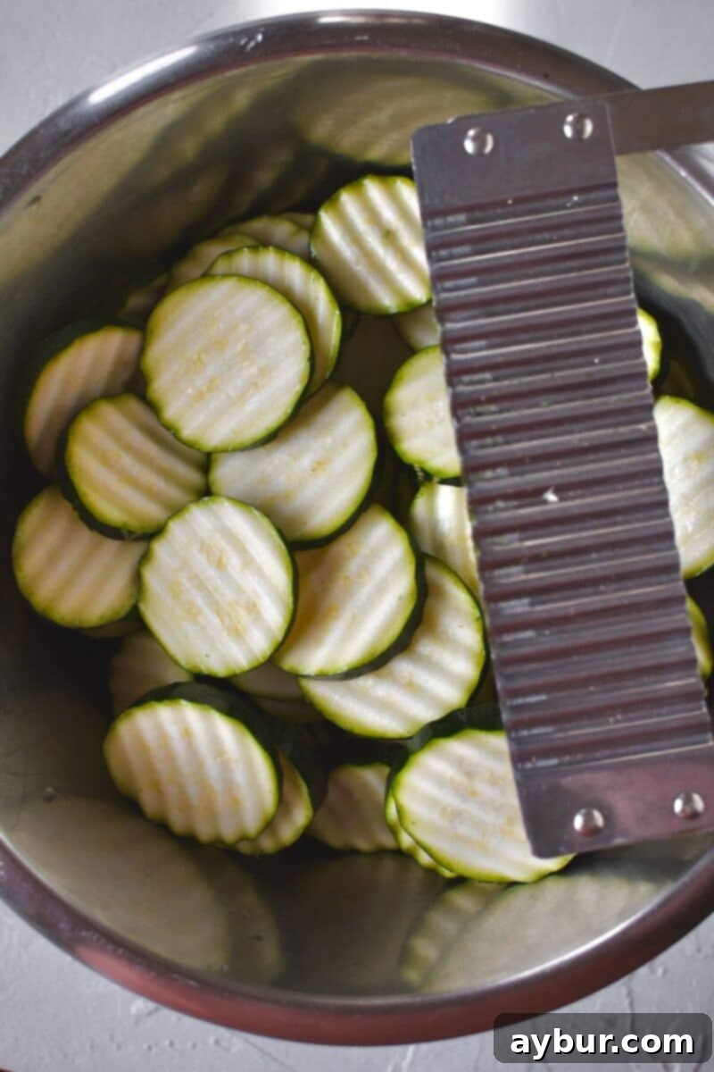 Baked Zucchini Crisps 4 Fresh zucchini, expertly sliced into uniform crinkle-cut coins, gathered in a bowl, awaiting the next step in preparation.