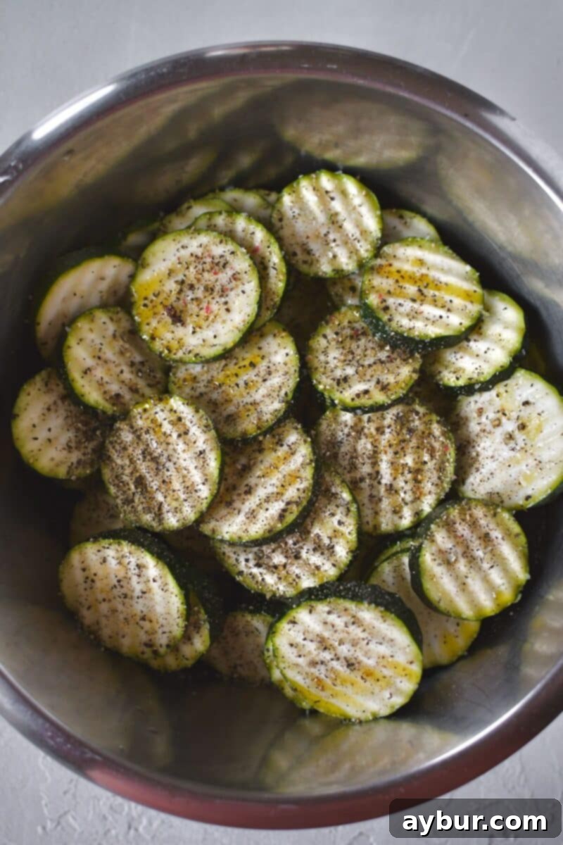 Baked Zucchini Crisps 5 Crinkle-cut zucchini slices in a bowl, generously drizzled with olive oil and seasoned with a sprinkle of salt and pepper, ready for tossing.