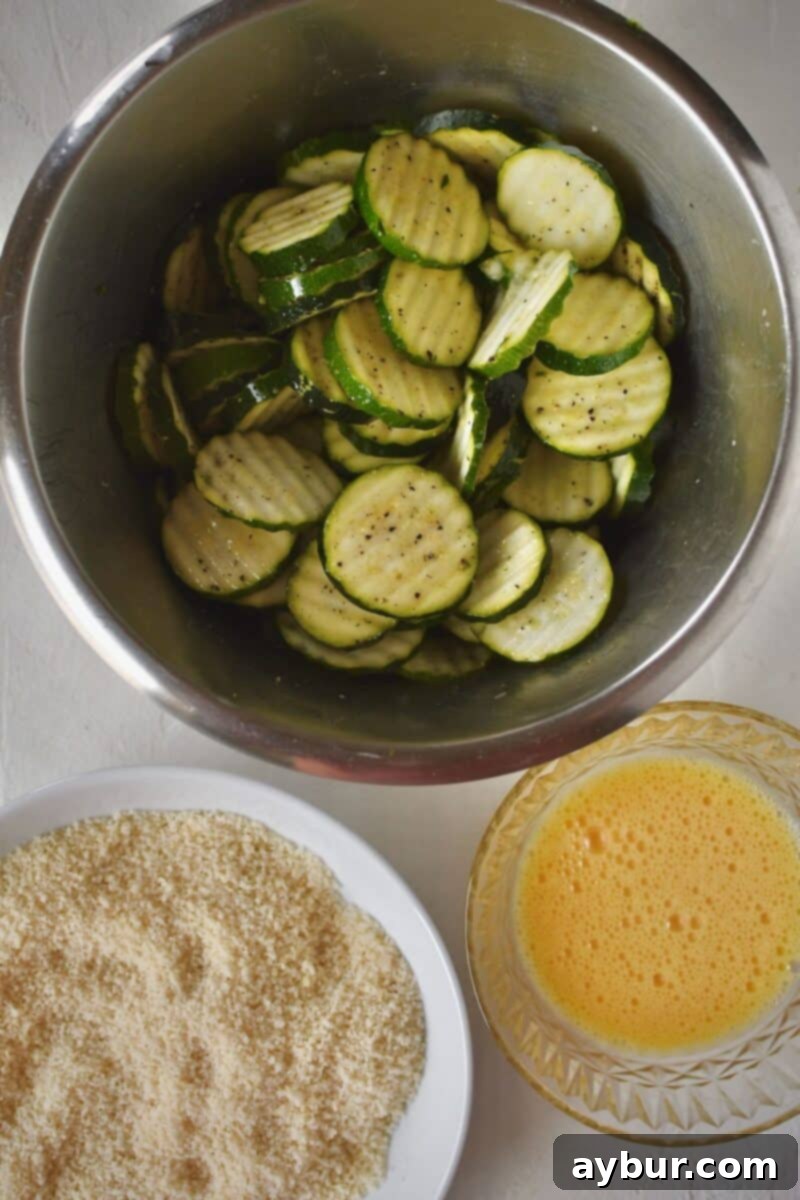 Baked Zucchini Crisps 7 A bowl of seasoned, sliced zucchini ready for the breading process, showcasing uniform cuts and a glistening coating of oil and spices.