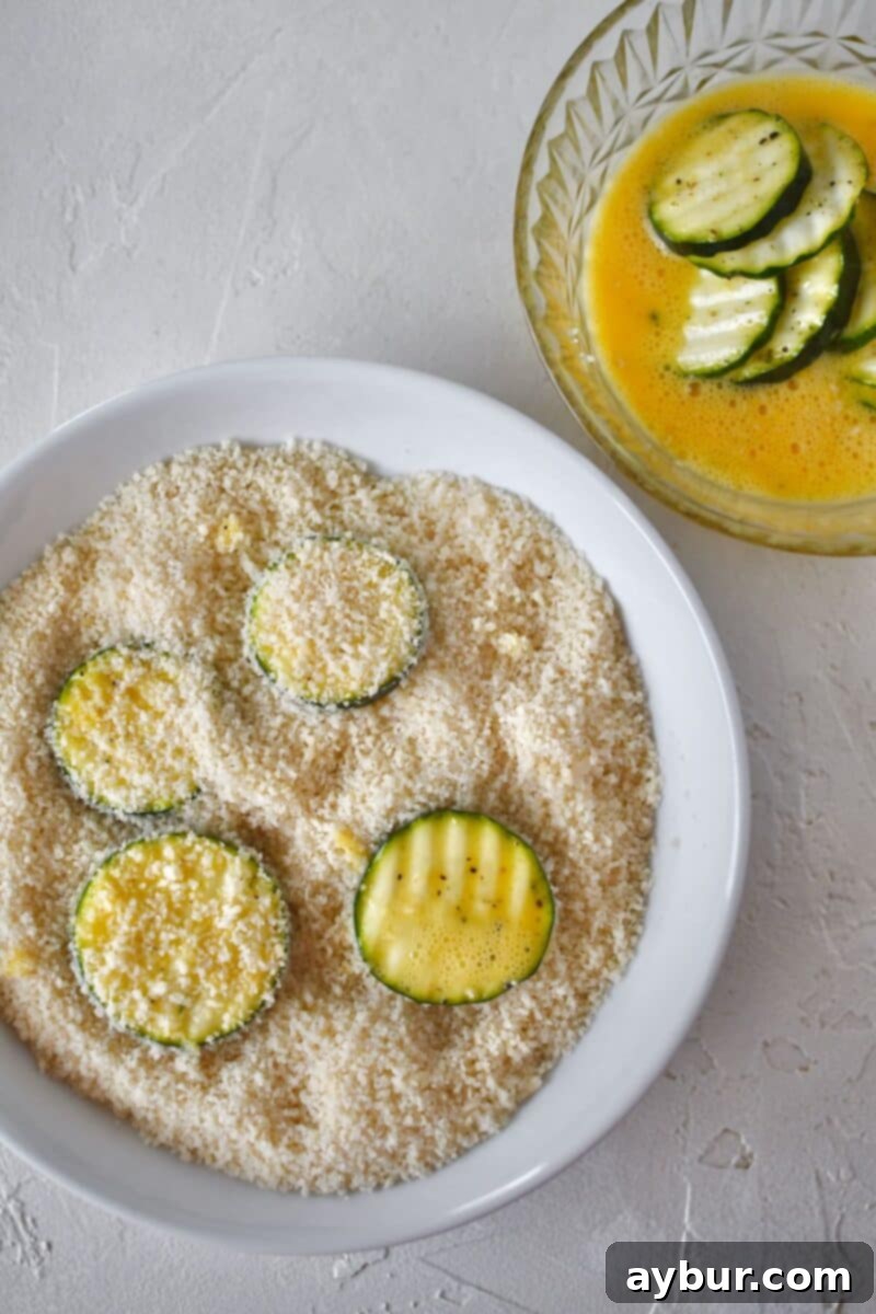 Baked Zucchini Crisps 8 A hand pressing a zucchini slice into the parmesan and panko mixture, ensuring a thick and even coating after it has been dipped in egg.