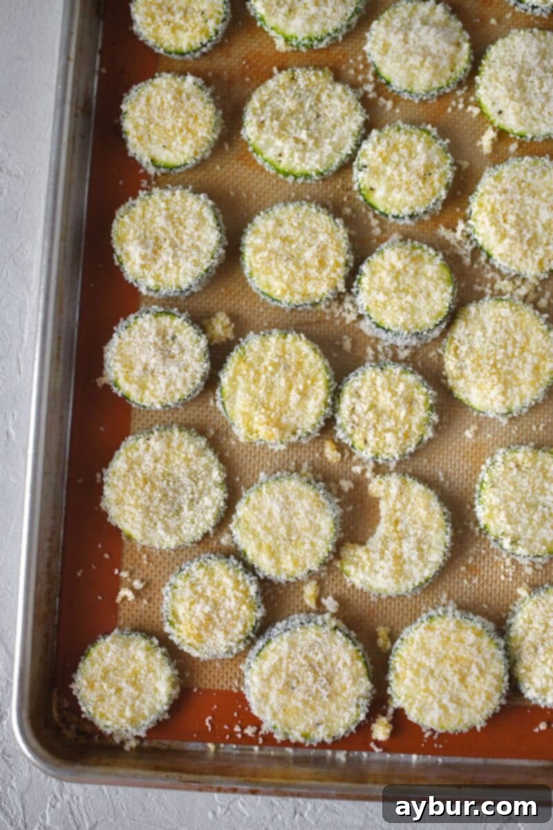 Baked Zucchini Crisps 9 Two baking sheets loaded with breaded zucchini chips arranged in a single layer, ready for the oven to bake to crispy perfection.