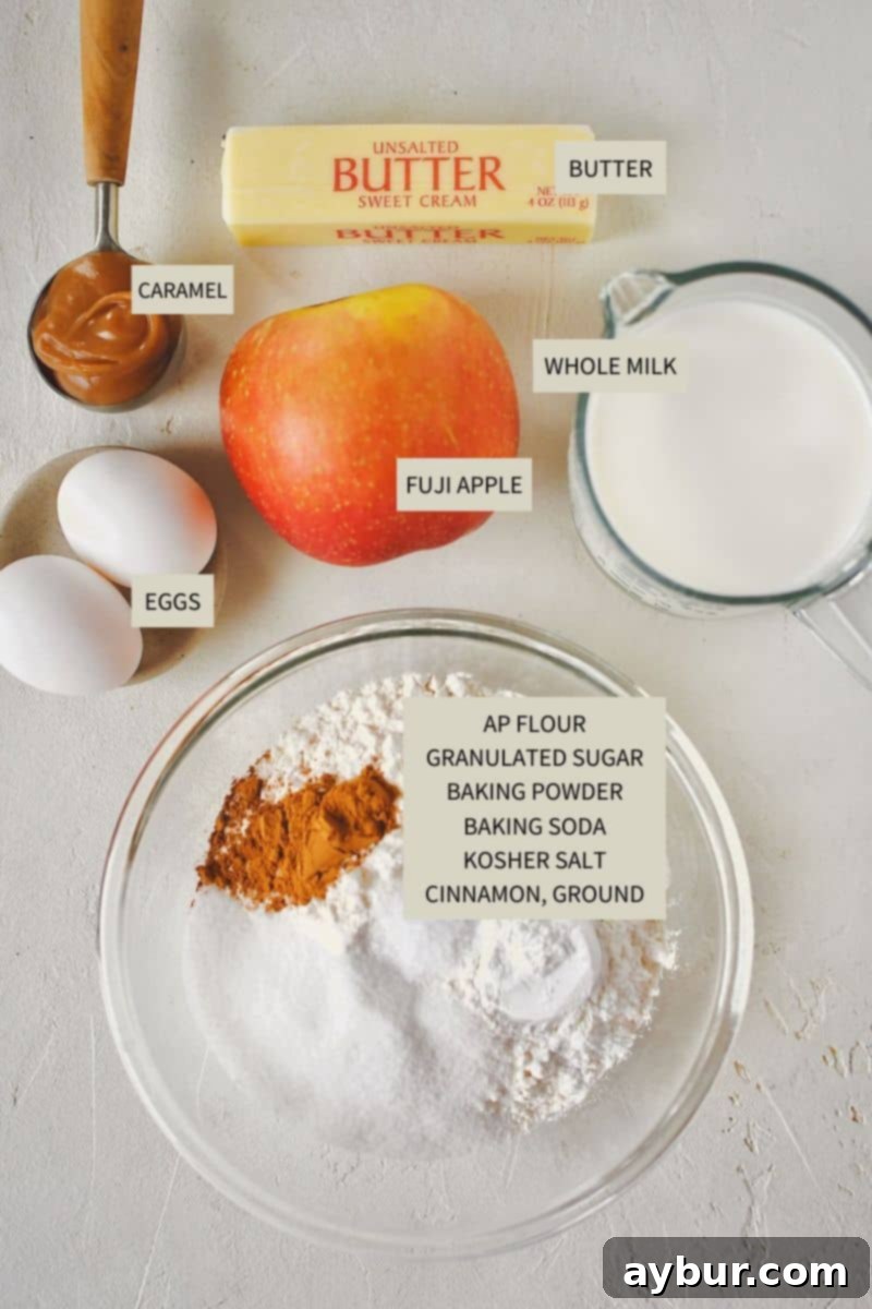 Warm Spiced Apple Pancakes 3 A selection of fresh ingredients laid out on a kitchen counter, including flour, milk, eggs, butter, baking powder, baking soda, salt, cinnamon, a whole Fuji apple, and a jar of caramel sauce, ready to make Apple Cinnamon Pancakes.