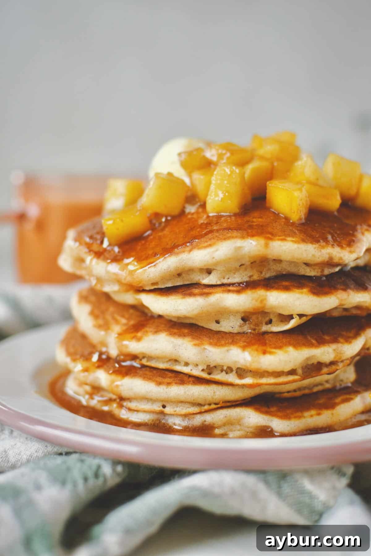 Warm Spiced Apple Pancakes 9 A close-up shot of Apple Cinnamon Pancakes, showcasing their fluffy texture and the rich, glossy caramel apple syrup cascading down the sides.