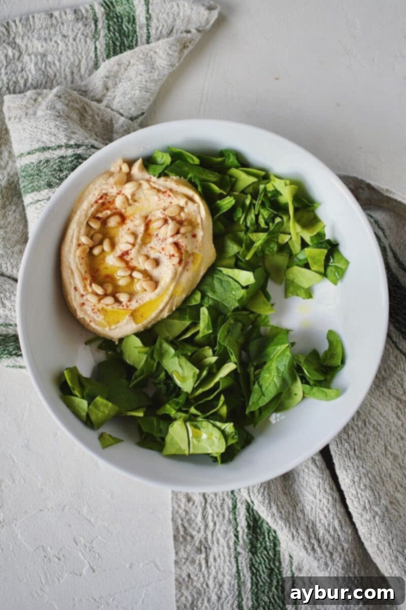 Beginning the assembly of a Mediterranean Bowl with a base of fresh spinach and a scoop of creamy hummus.