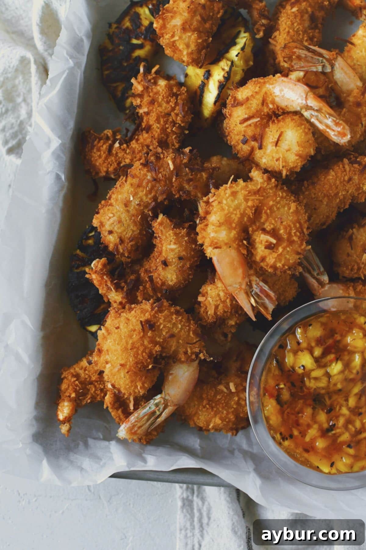 A close-up of a perfectly fried Coconut Shrimp, showcasing its golden-brown, crispy exterior and succulent interior, with a light bokeh background.
