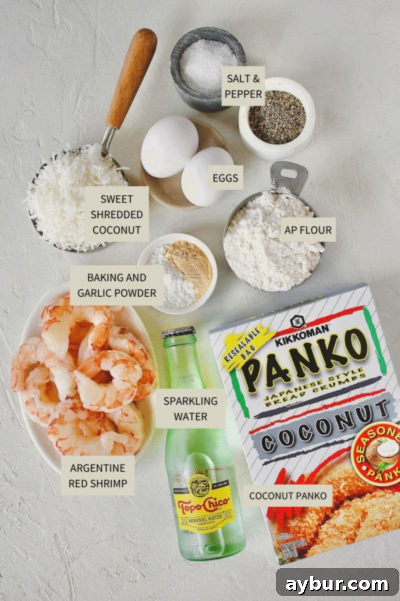 A selection of fresh ingredients laid out for making Coconut Shrimp, including shrimp, flour, eggs, sparkling water, panko, and shredded coconut.