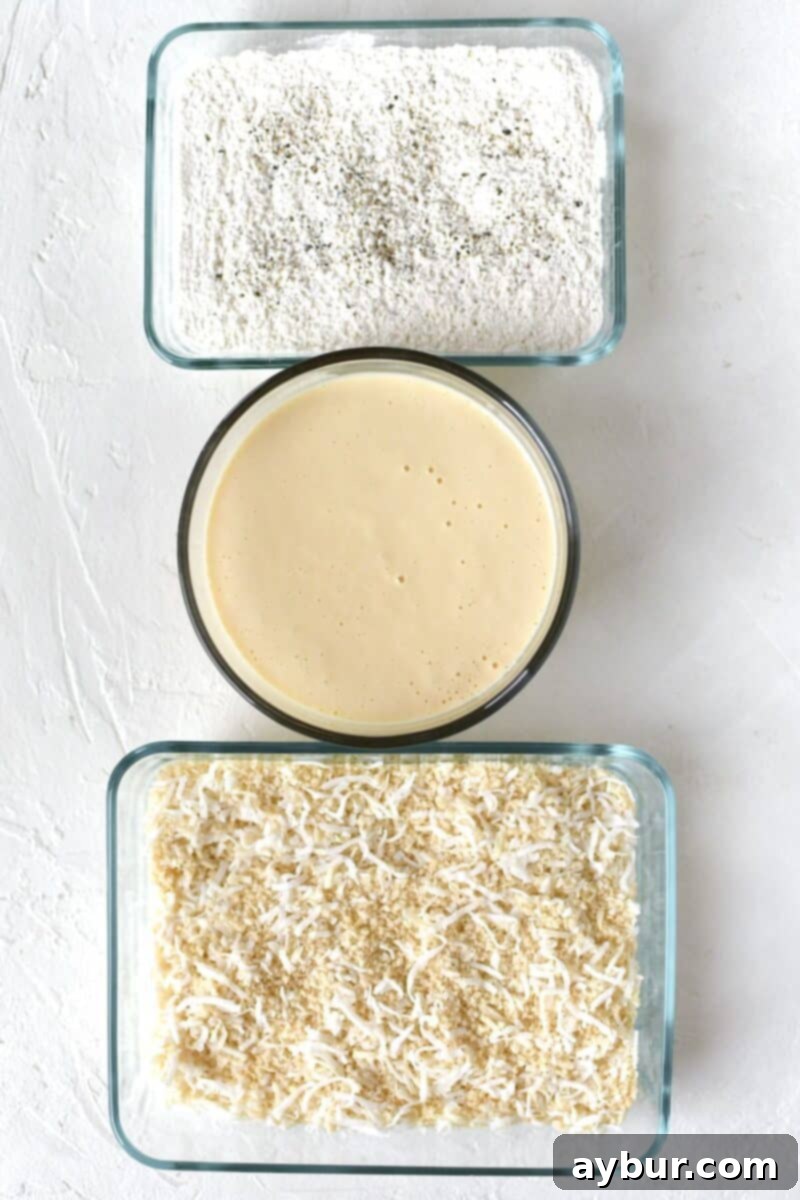 An organized breading station with three bowls: one for seasoned flour, one for the wet batter, and one for the coconut panko breading mixture, ready for coating shrimp.
