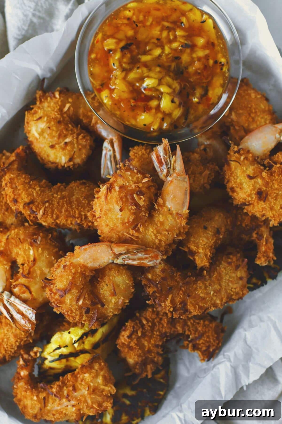 A vibrant platter of crispy Fried Coconut Shrimp, garnished with fresh cilantro and served alongside a bowl of sweet chili dipping sauce and grilled pineapple slices.