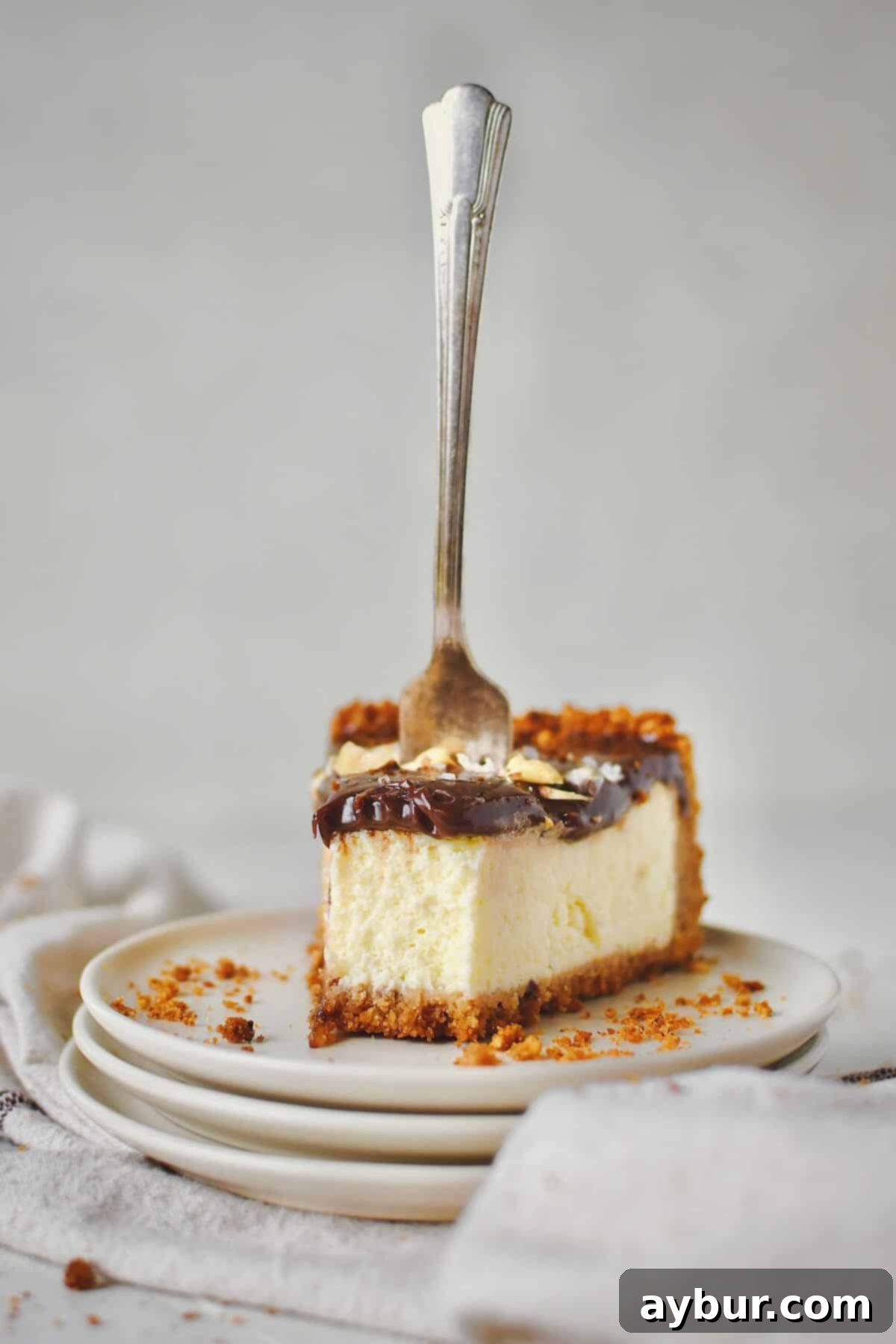 A single slice of Italian Cheesecake on a plate, with a bite taken out and a fork resting in it, showcasing its light, creamy texture and hazelnut crust.