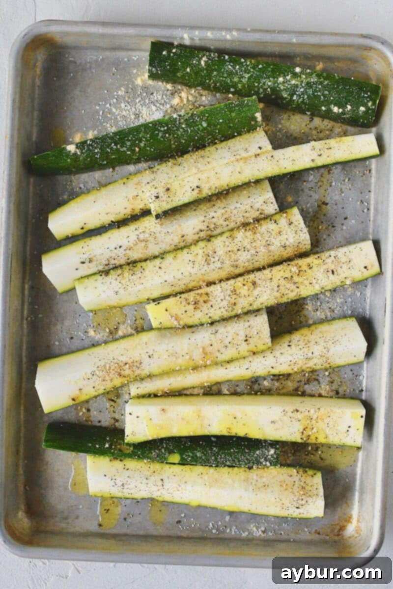 Quartered zucchini on a sheet pan, drizzled with olive oil and spices before tossing.