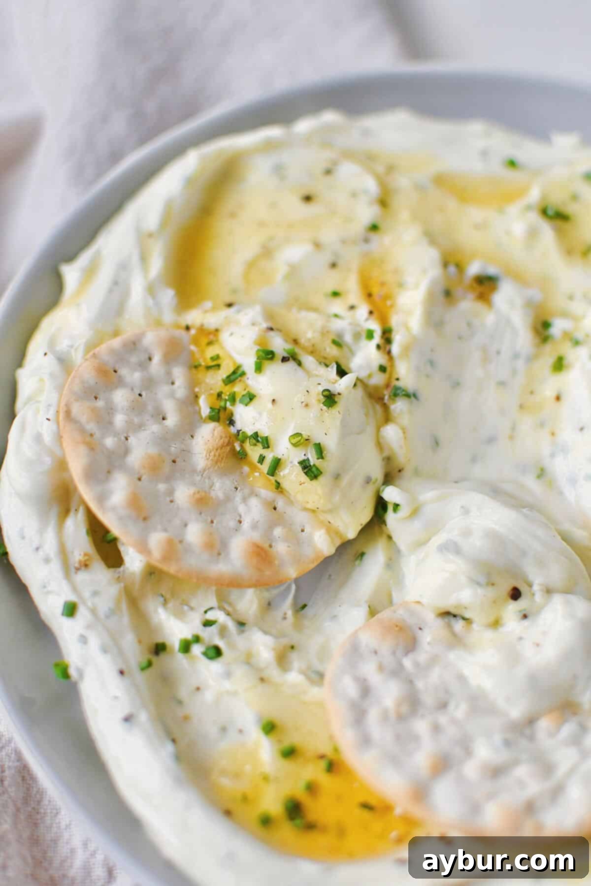 Velvet Goat Cheese Spread 2 Whipped Goat Cheese spread on a plate and topped with lavender honey, chives, and sea salt. Cracker being dipped in.