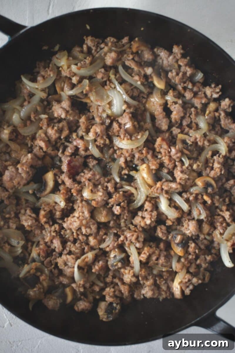 Button mushrooms and onions browned with italian sausage in a large skillet.