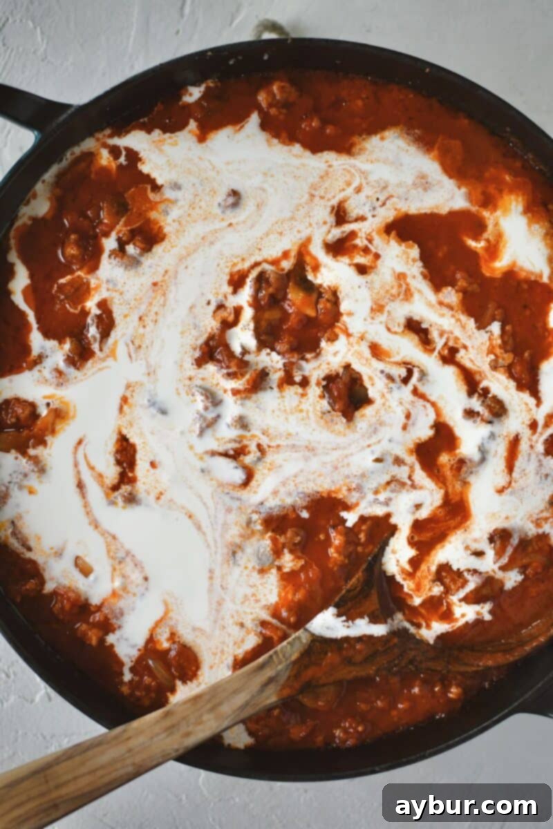 Stirring in the marinara and heavy cream into the browned sausage, onions, and mushrooms to form a decadent pasta sauce.