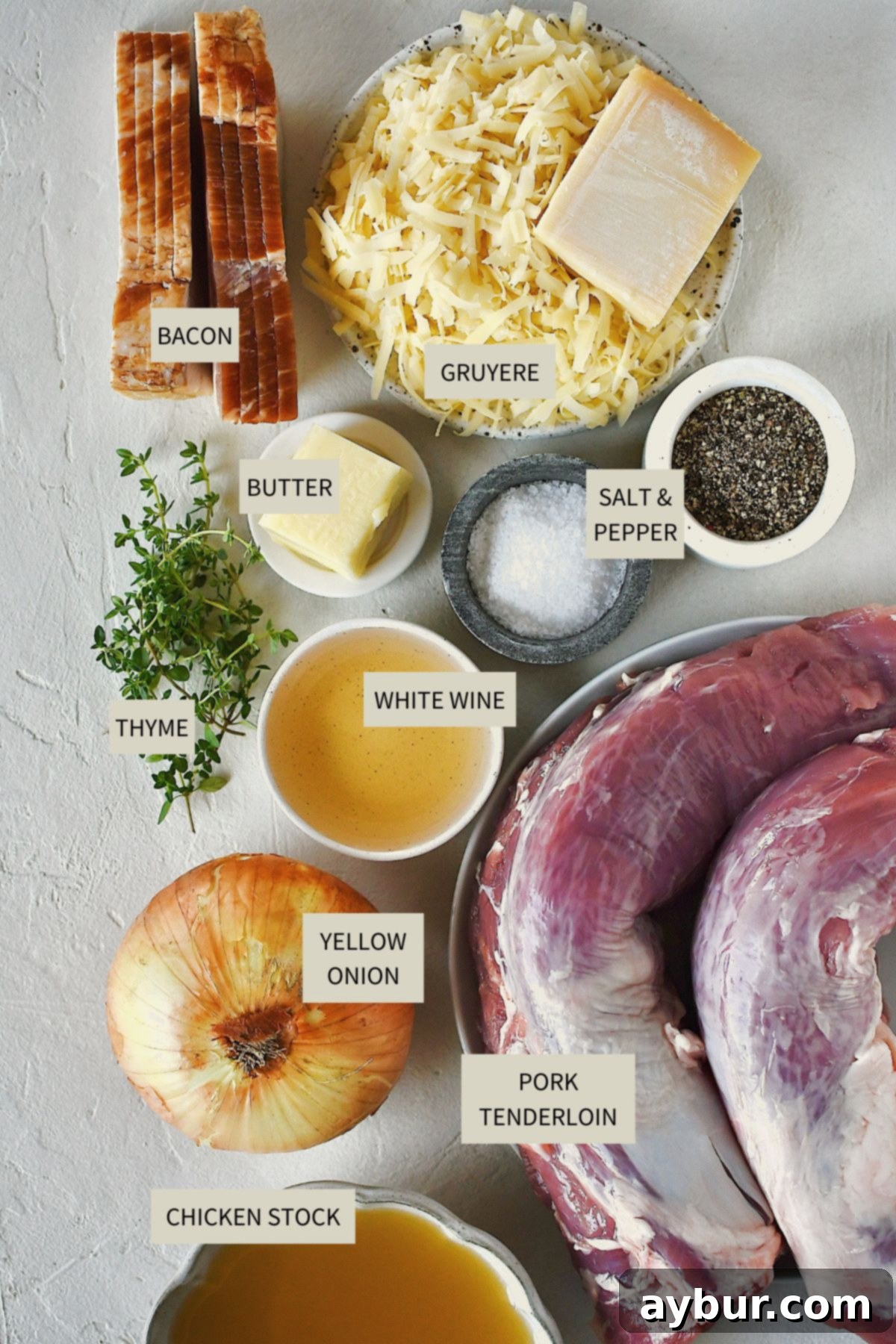 Savory Stuffed Pork Tenderloin 3 A display of fresh ingredients including pork tenderloins, yellow onions, Gruyère cheese, bacon, white wine, and thyme, ready for making Stuffed Pork Tenderloin.