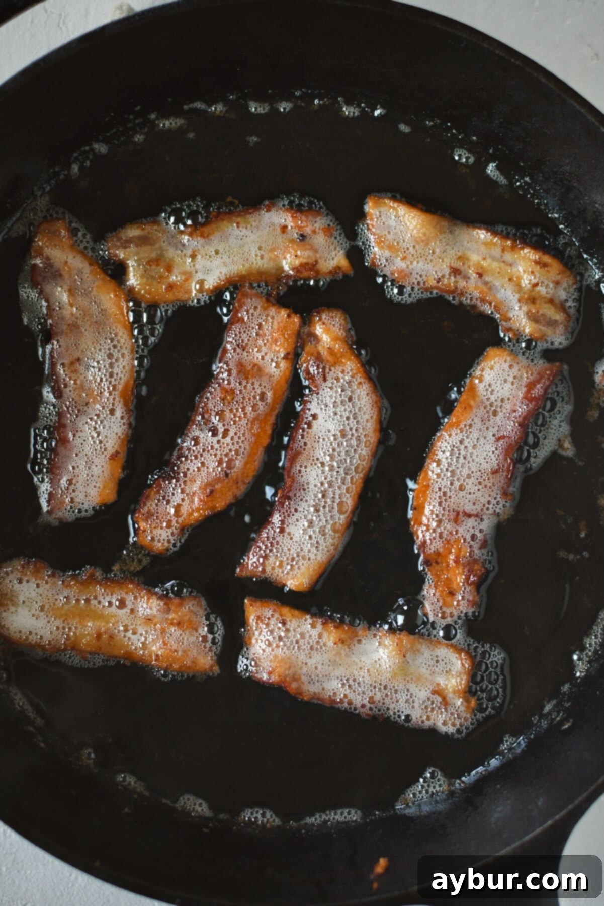 Savory Stuffed Pork Tenderloin 4 Crispy bacon sizzling and cooking in a large cast iron skillet, rendering fat for the Stuffed Pork Tenderloin.