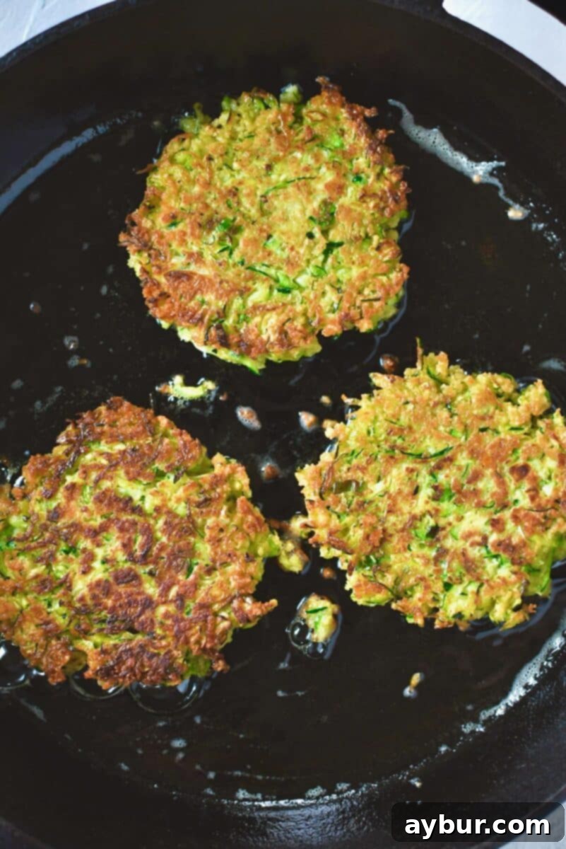 Golden zucchini fritters after flipping, cooking the second side till golden.