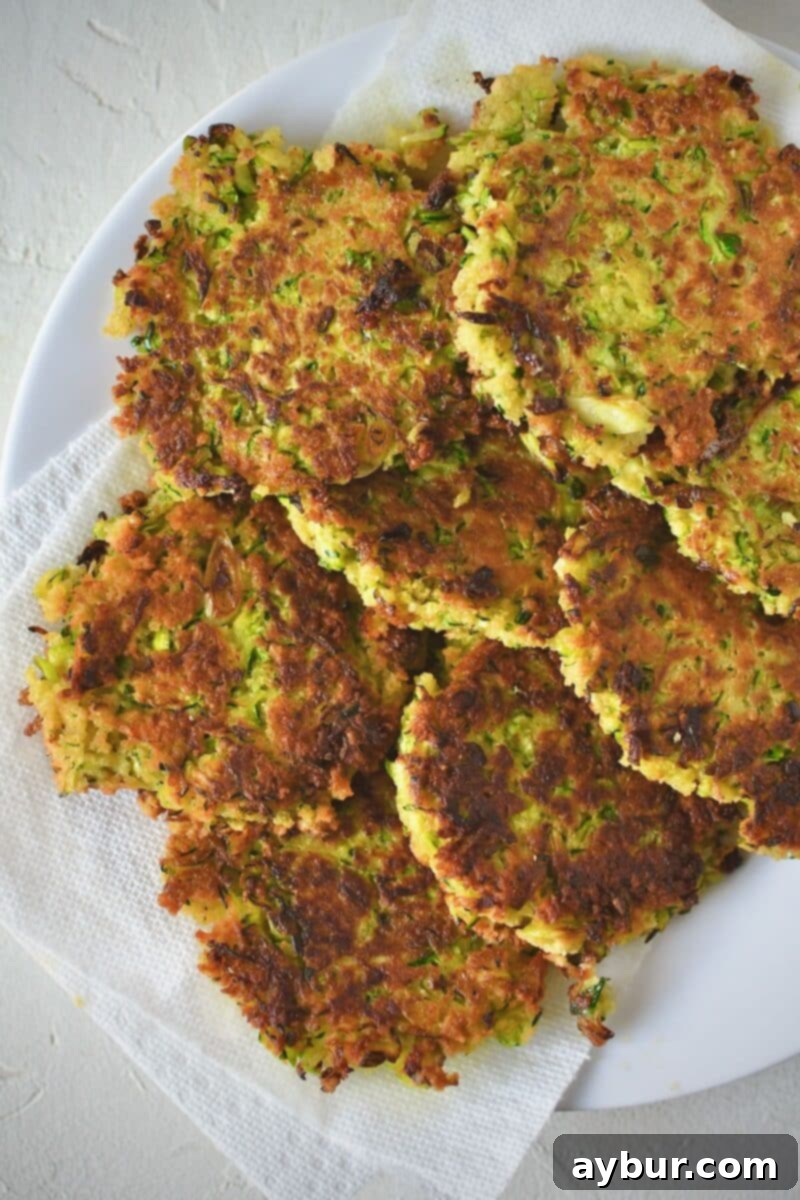 Zucchini fritters after frying, resting on a paper towel lined plate.