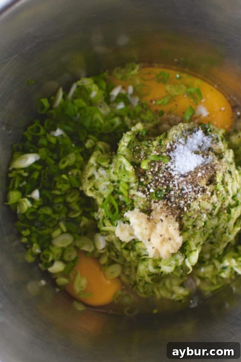 Adding the squeezed zucchini to a bowl with the egg, salt, pepper, garlic, and green onions.