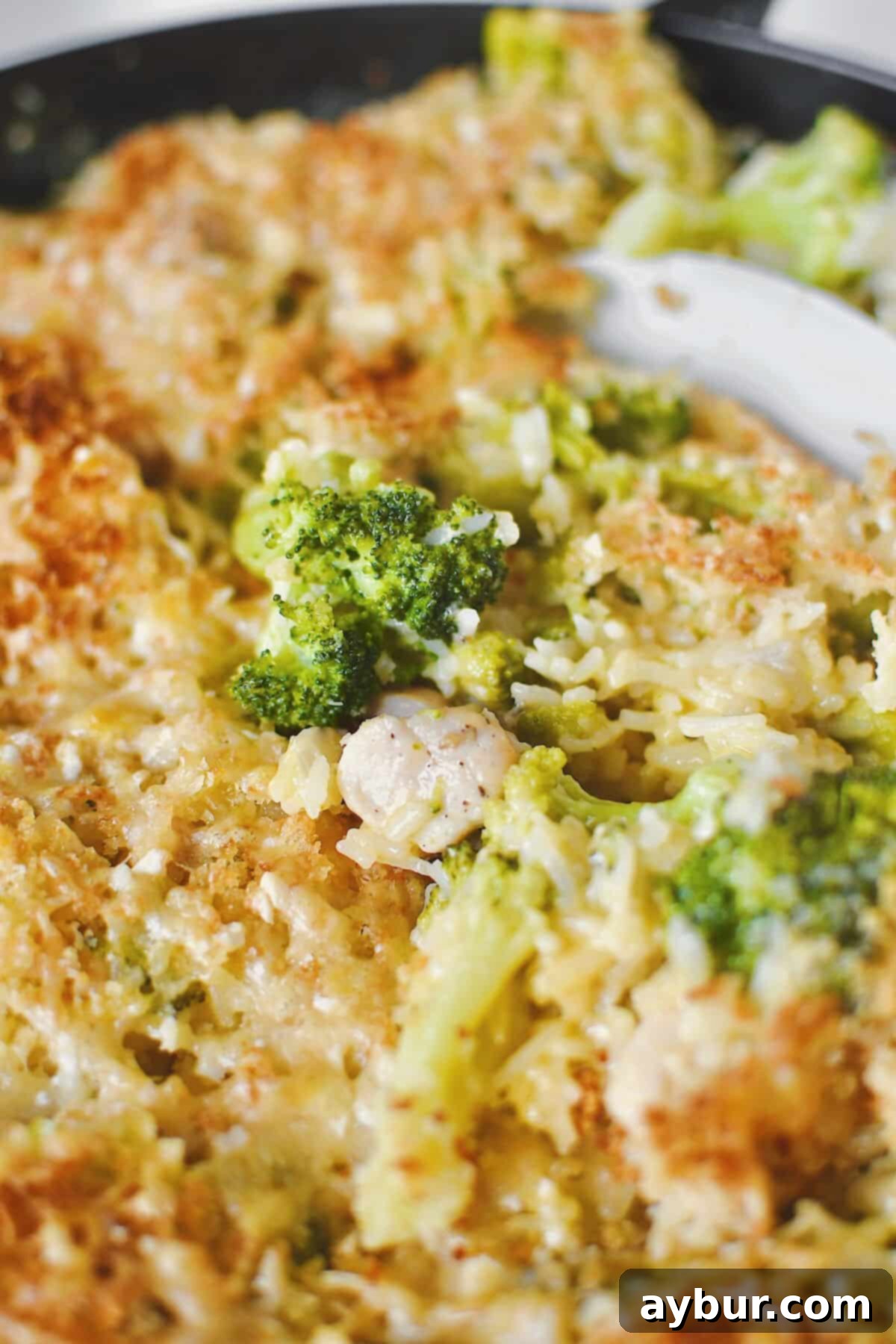 Fırında Tavuklu Brokoli Pilavı 13 A close-up shot of a serving spoon scooping out a generous portion of the golden-brown and bubbly Chicken and Broccoli Rice Casserole.