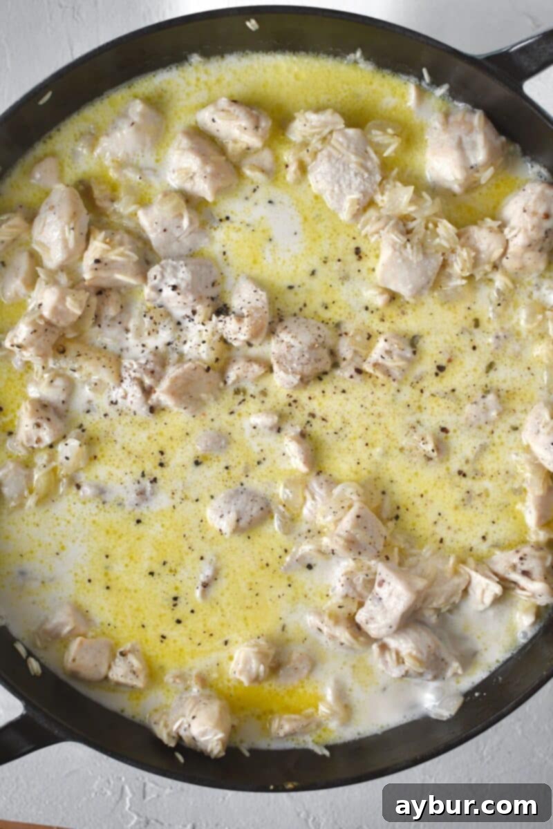 Fırında Tavuklu Brokoli Pilavı 6 A creamy sauce is forming in the pan as chicken stock, heavy cream, milk, and seasonings are added and stirred into the rice and chicken mixture.