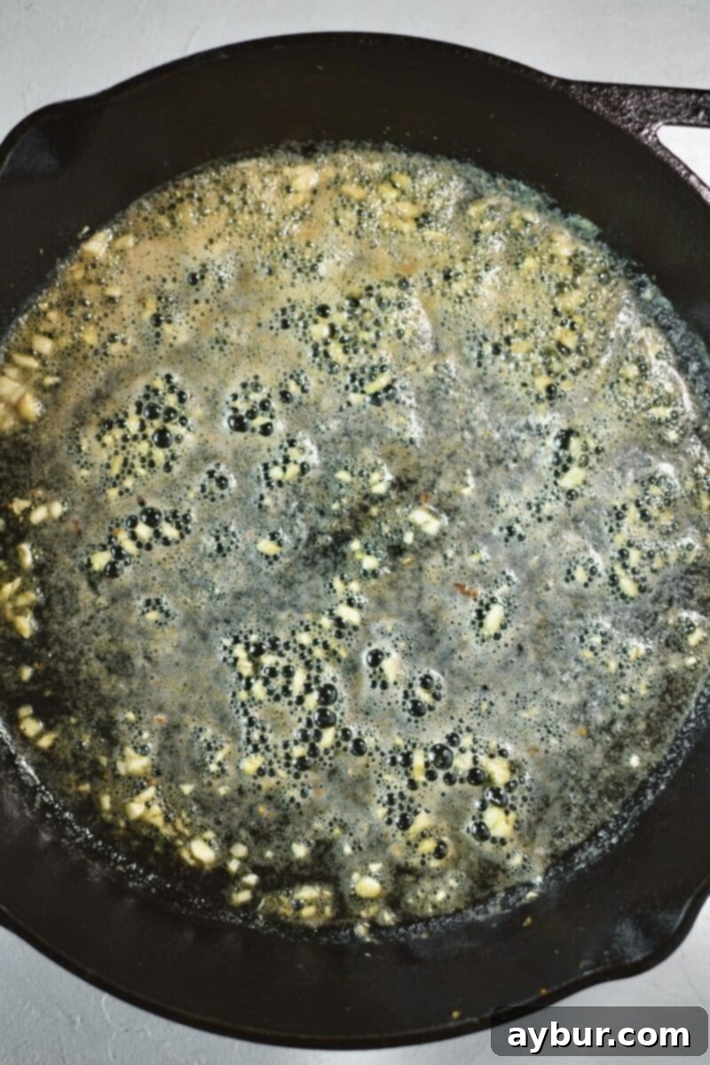 Creamy Green Beans 4 Garlic cooking in butter in a large cast iron skillet on the stove.