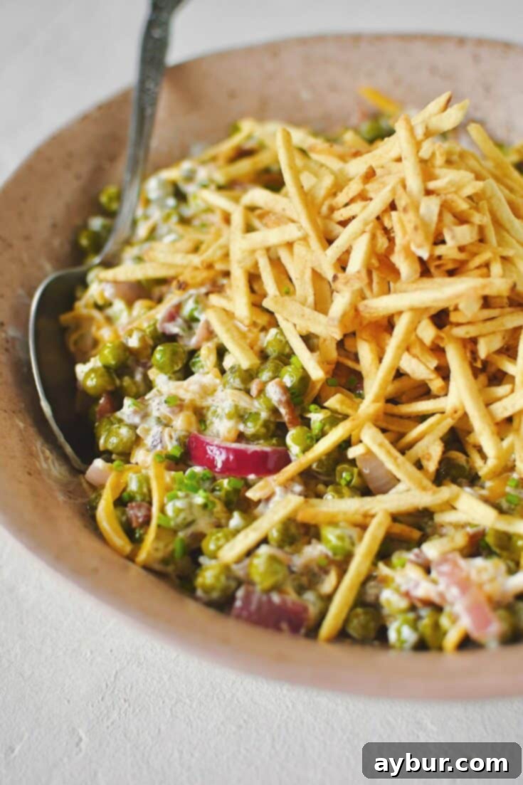 Pea Salad 12 Bacon Pea Salad tossed together in a bowl and topped with shoestring potatoes.