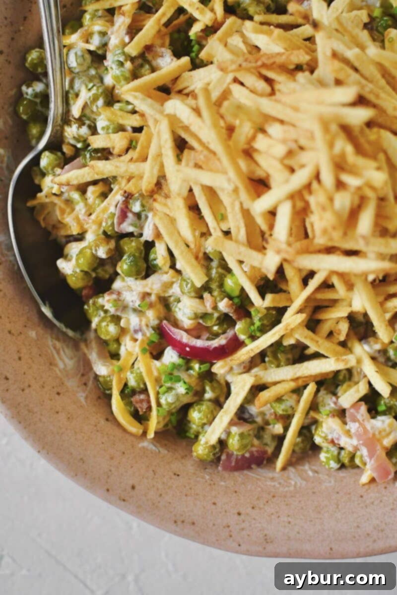 Pea Salad 8 Close-up of the completed Bacon Pea Salad, showing the mix of peas, bacon, cheese, and a generous topping of golden shoestring potatoes in a serving bowl.