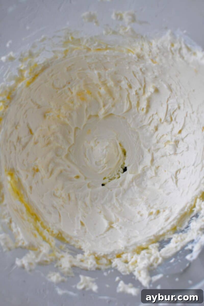 Close-up of smooth, whipped cream cheese in a stand mixer bowl, ready for the next ingredients.