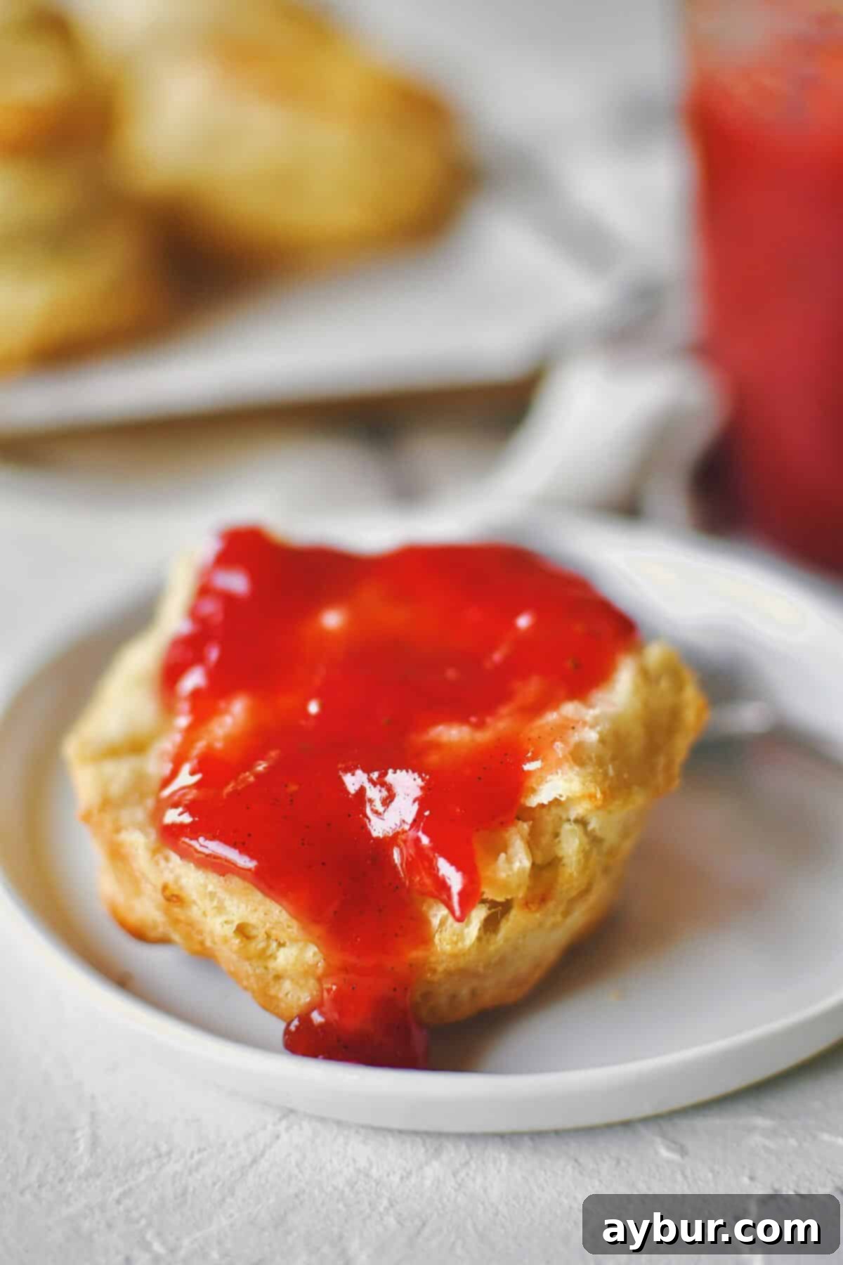 Sun-Kissed Strawberry Rhubarb Spread 2 Freshly made Strawberry Rhubarb Jam being spread generously on a warm, homemade biscuit.