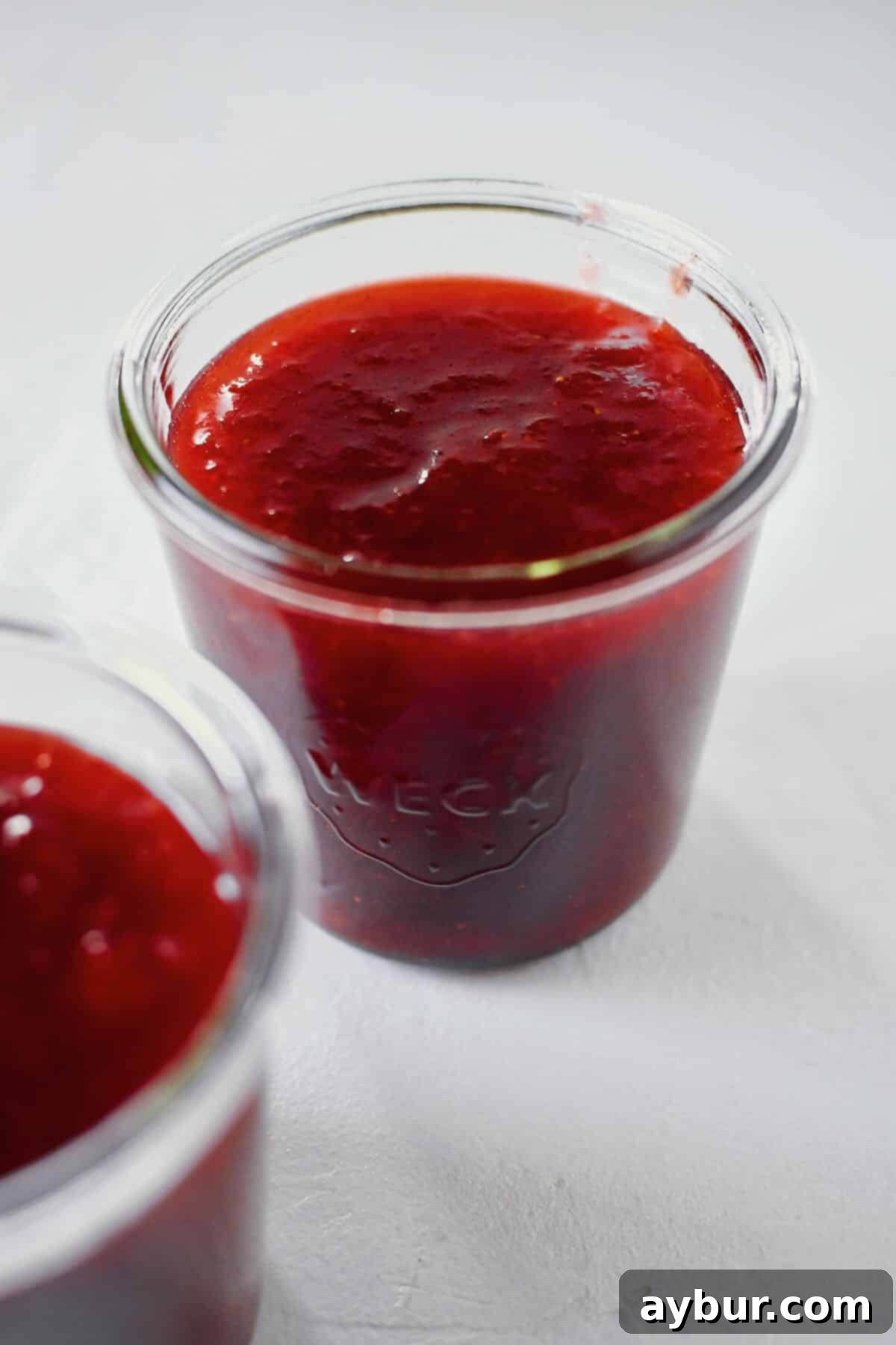 Sun-Kissed Strawberry Rhubarb Spread 11 Freshly cooked Strawberry Rhubarb Jam neatly poured into several sterilized glass jars, showcasing its rich color and smooth texture, ready for cooling and refrigeration.