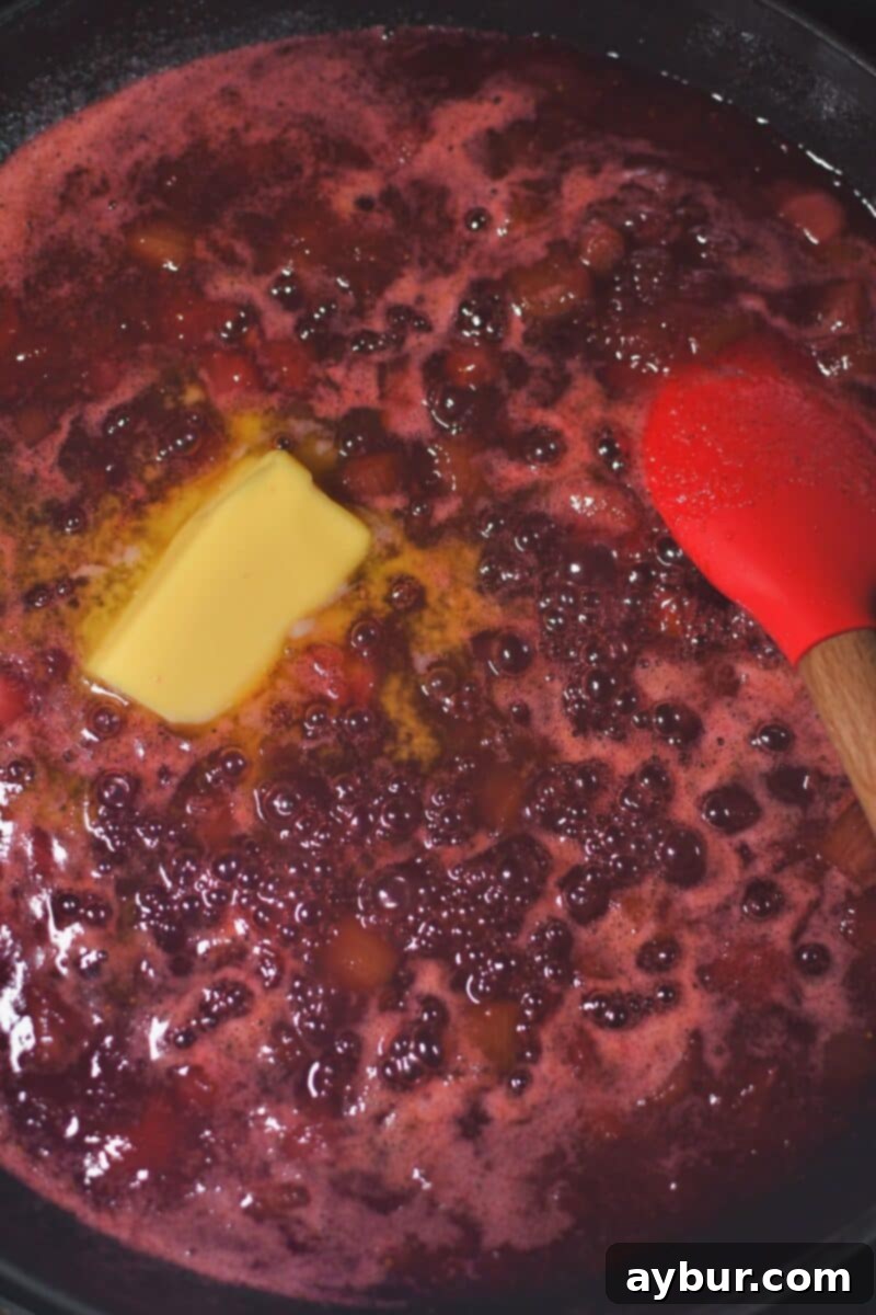 Sun-Kissed Strawberry Rhubarb Spread 8 The jam mixture, now visibly thickened after cooking, with the butter just added and beginning to melt into the fruit, promising a smooth and rich consistency.