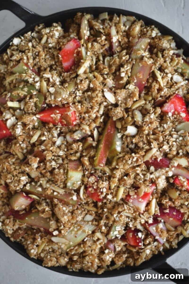 A fully assembled Strawberry Rhubarb Crisp, with a generous layer of oat and almond topping over the fruit filling, ready for baking in the oven.