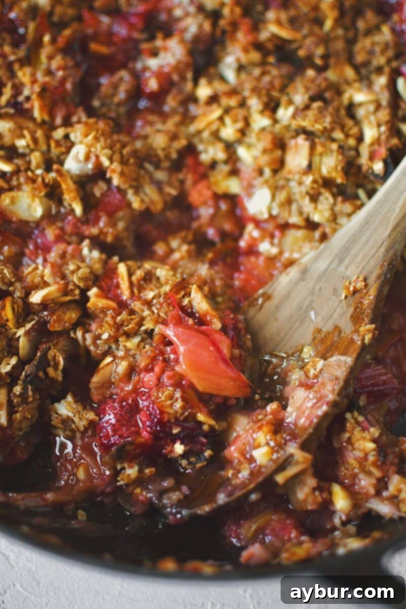 A warm, freshly baked Strawberry Rhubarb Crisp being scooped out of the baking dish, steam rising, ready to be served.