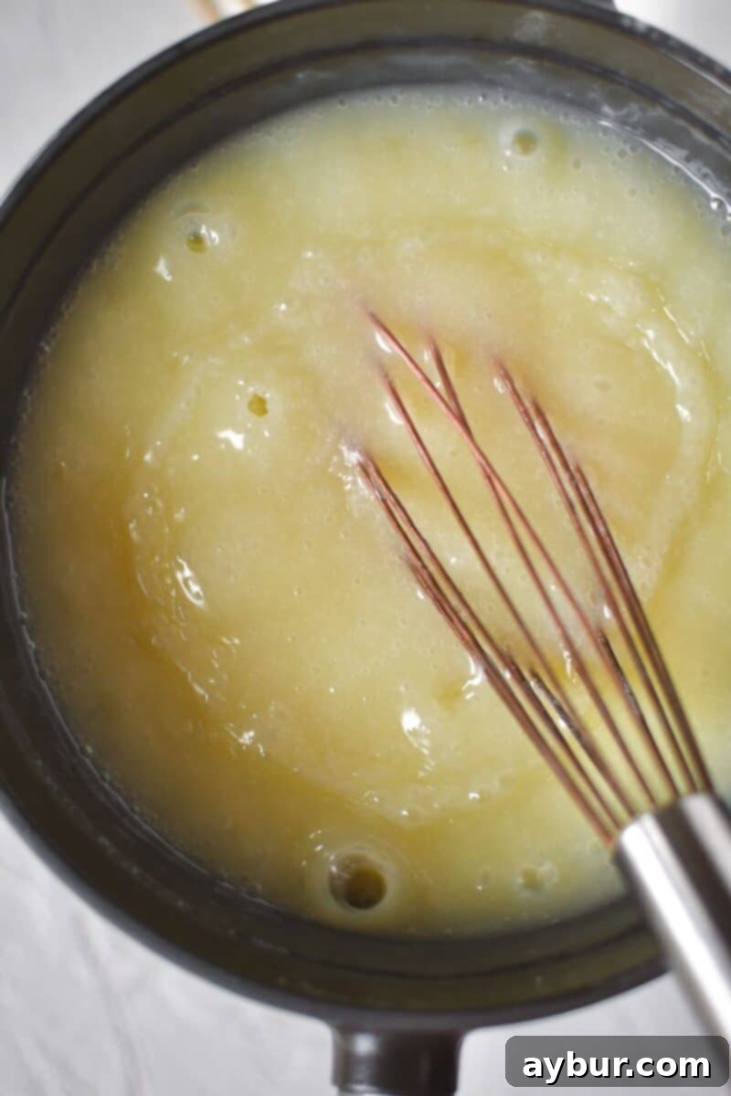 Strawberry Delight 5 Vigorously whisking the boiling ice cream base in a saucepan, a mixture of cream, sugar, and corn syrup, to ensure uniform heating and dissolution of sugar.
