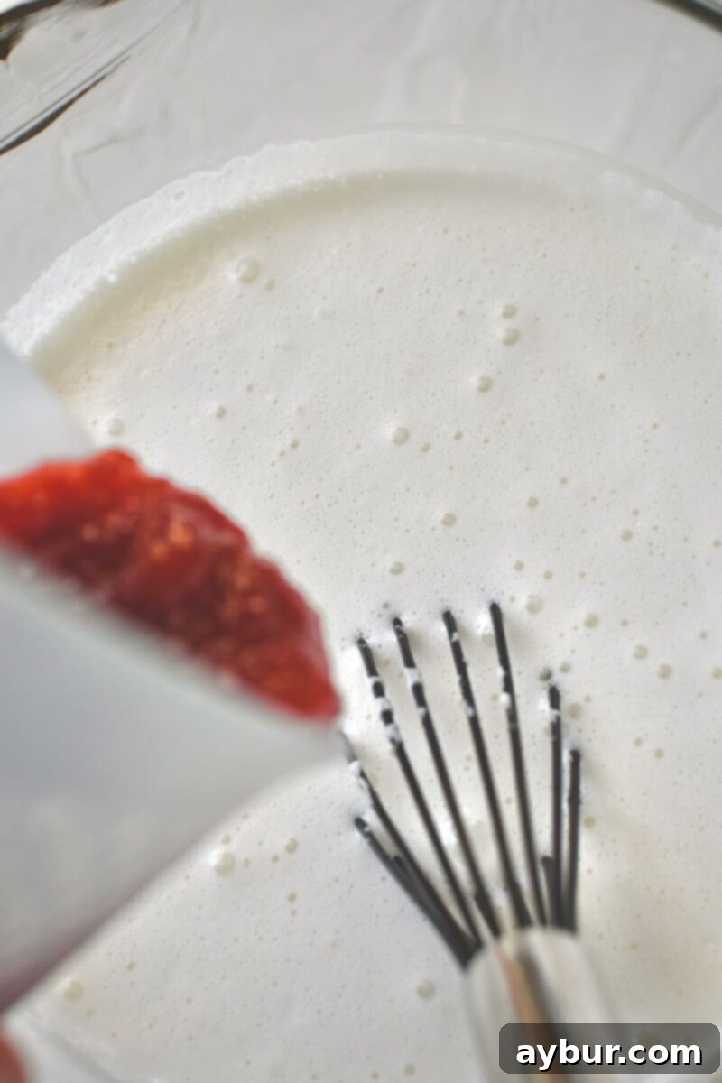 Strawberry Delight 7 Adding luscious strawberry rhubarb jam to the smooth ice cream base in a blender, ready to be incorporated for vibrant flavor and color.