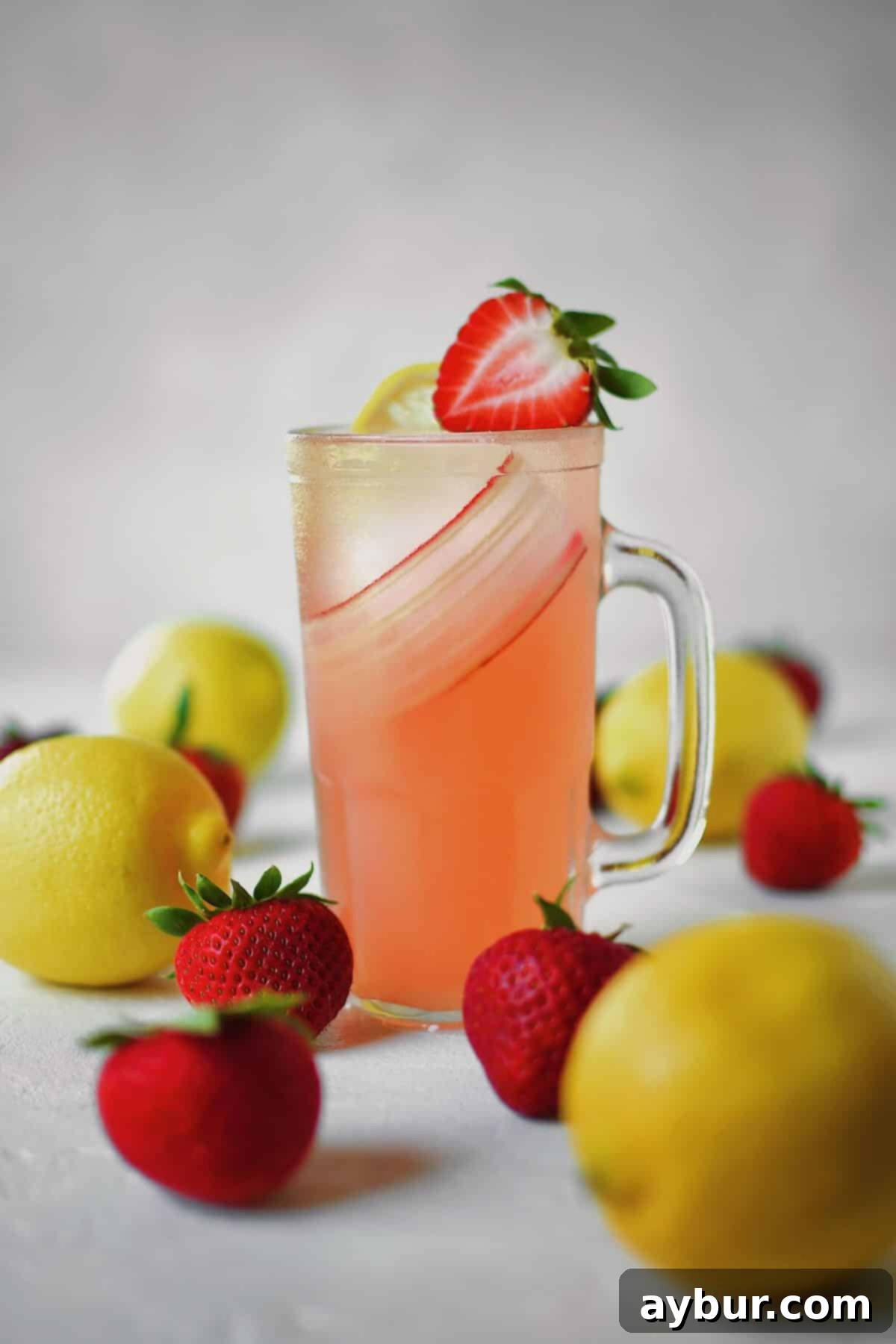 Sweet Strawberry Lemonade 2 A glass of strawberry lemonade on a table with fresh strawberries and lemons around it.