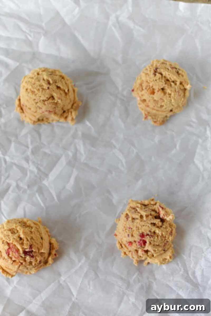 Portioned mounds of cookie dough, ready to be filled, arranged neatly on a parchment-lined sheet pan.
