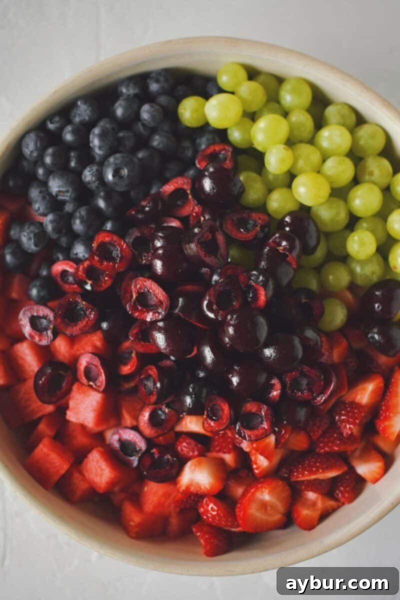 A large mixing bowl filled with an colorful assortment of diced watermelon, grapes, and various berries, ready for the dressing.
