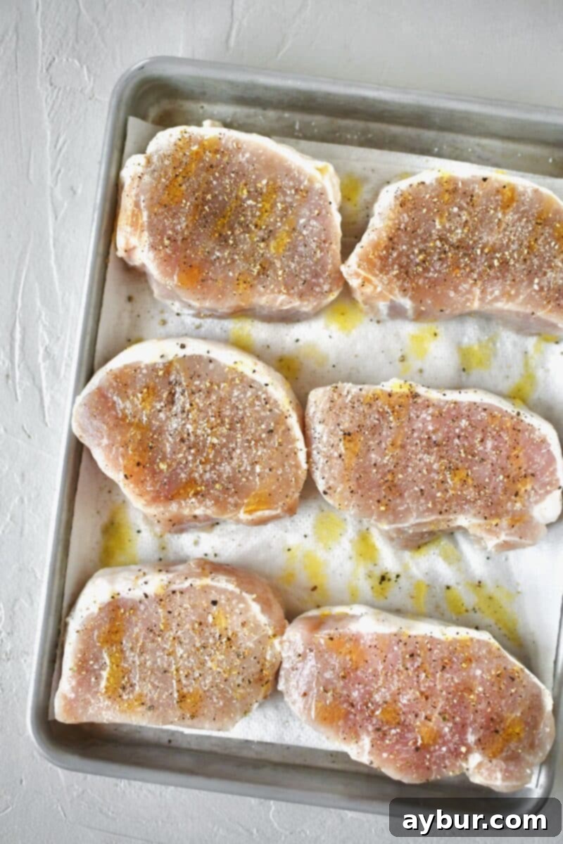 Brined pork chops, freshly patted dry with paper towels, seasoned with olive oil, salt, and pepper, awaiting cooking.