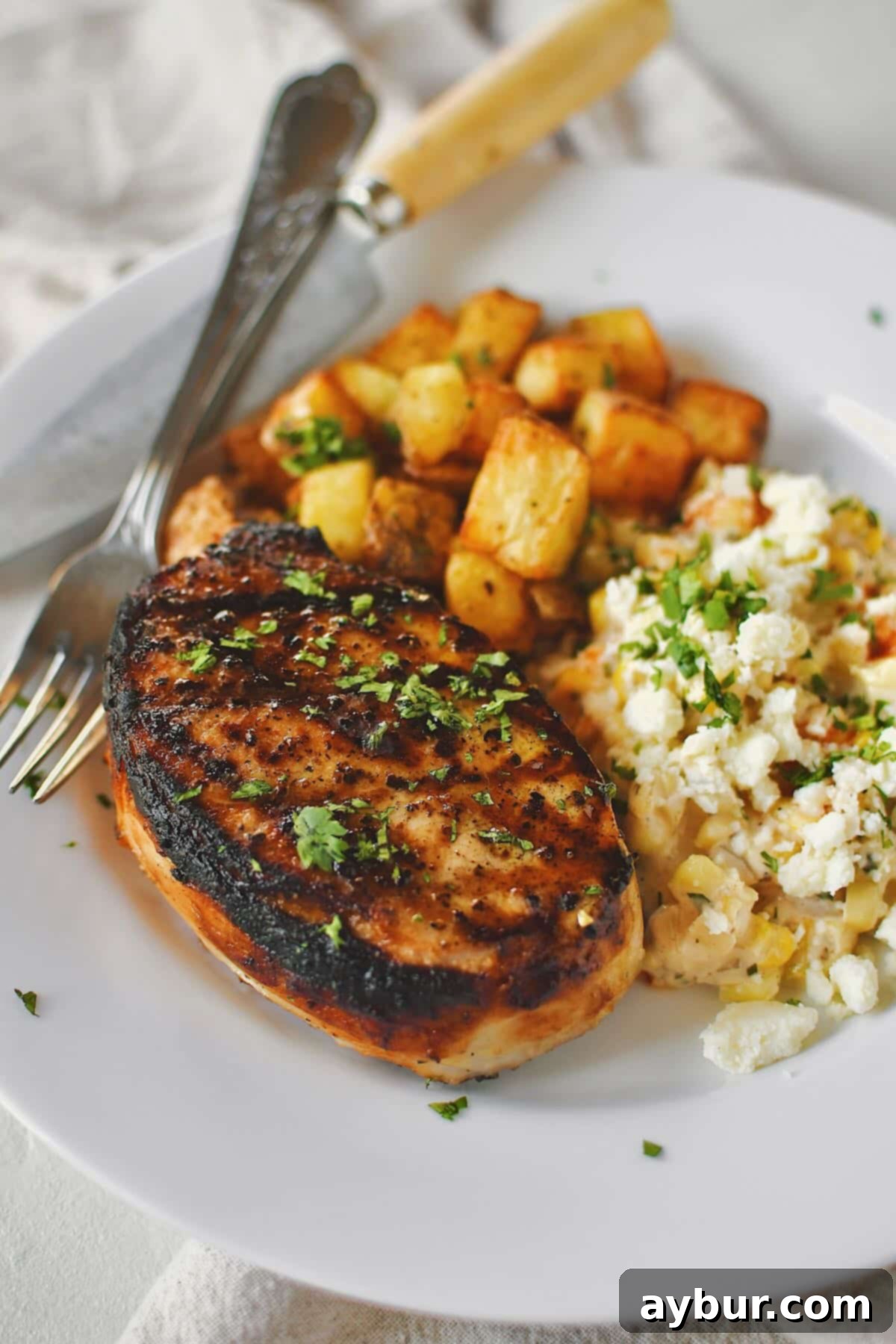 Beautifully brined pork chops, freshly grilled, served alongside roasted potatoes and corn on the cob, creating a perfect balanced meal.