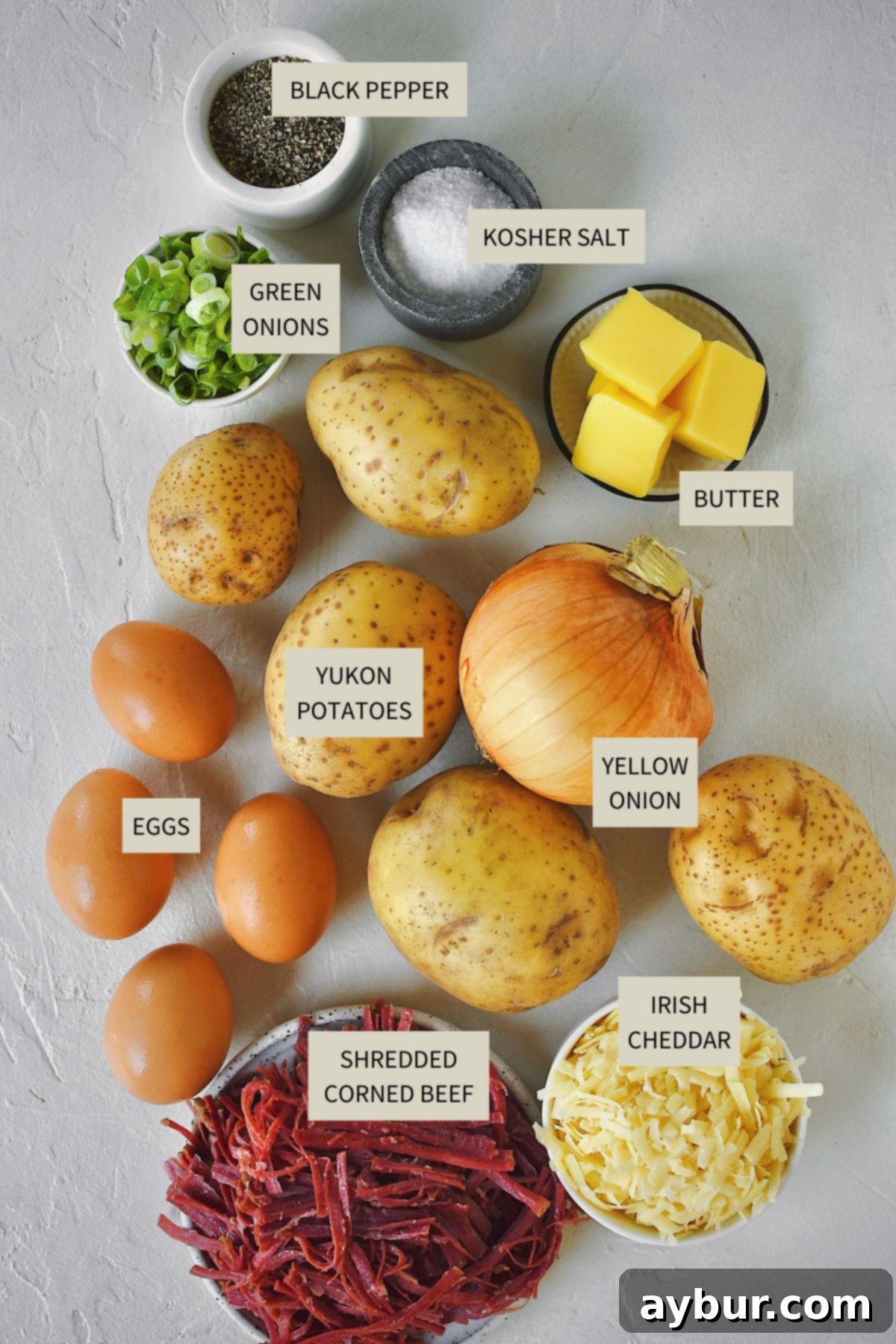 A vibrant display of fresh ingredients: diced Yukon Gold potatoes, sliced yellow onion, Irish butter, shredded corned beef, fresh eggs, and Irish white cheddar cheese, ready for the perfect corned beef hash.