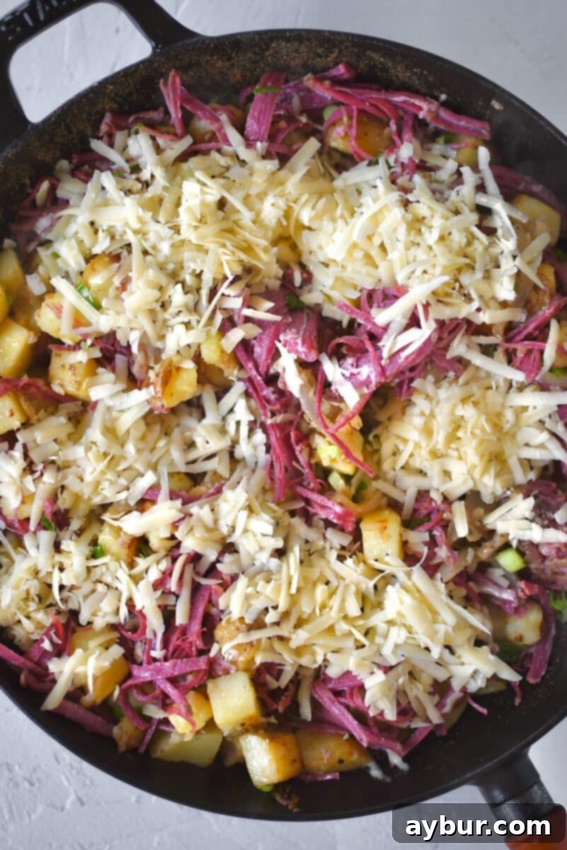 Tender shredded corned beef is gently folded into the crispy potato and onion mixture, then topped with a generous layer of Irish white cheddar cheese, melting beautifully into the hash.