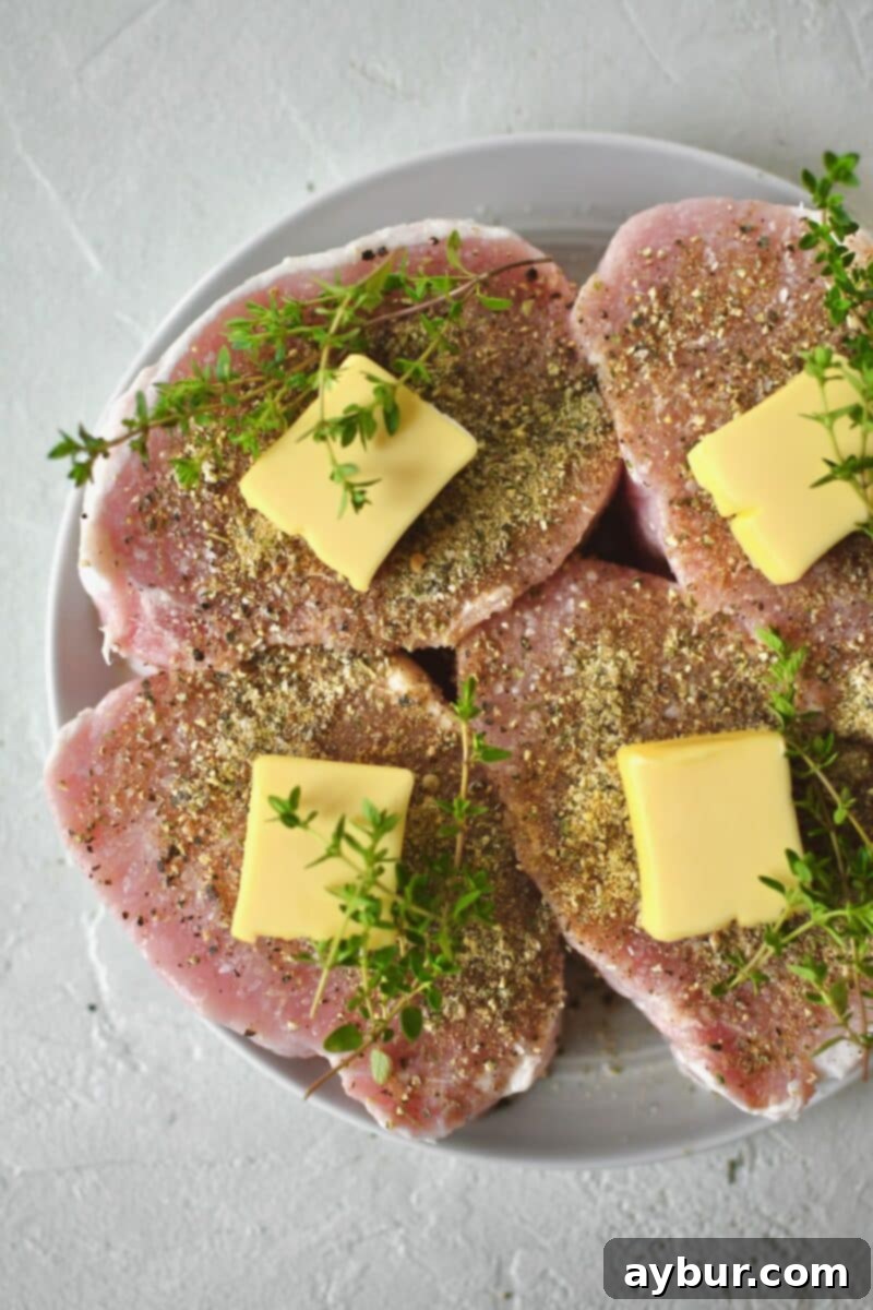 Perfectly Tender Sous Vide Pork Chops 5 Pork Chops seasoned on both sides with salt and pepper and steak seasoning and resting on a plate. Topped with butter and thyme sprigs.