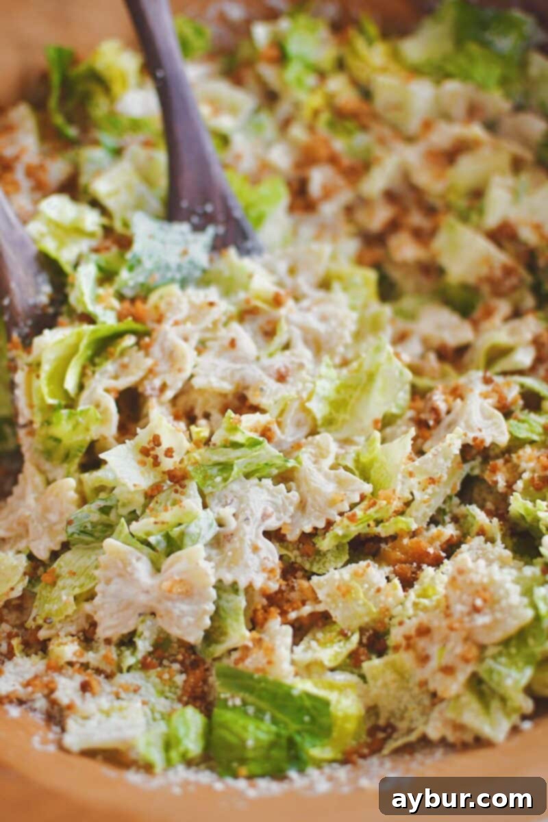 Close-up of Caesar Pasta Salad in a large bowl, showcasing the textures of pasta, romaine, and toasted breadcrumbs mixed together.