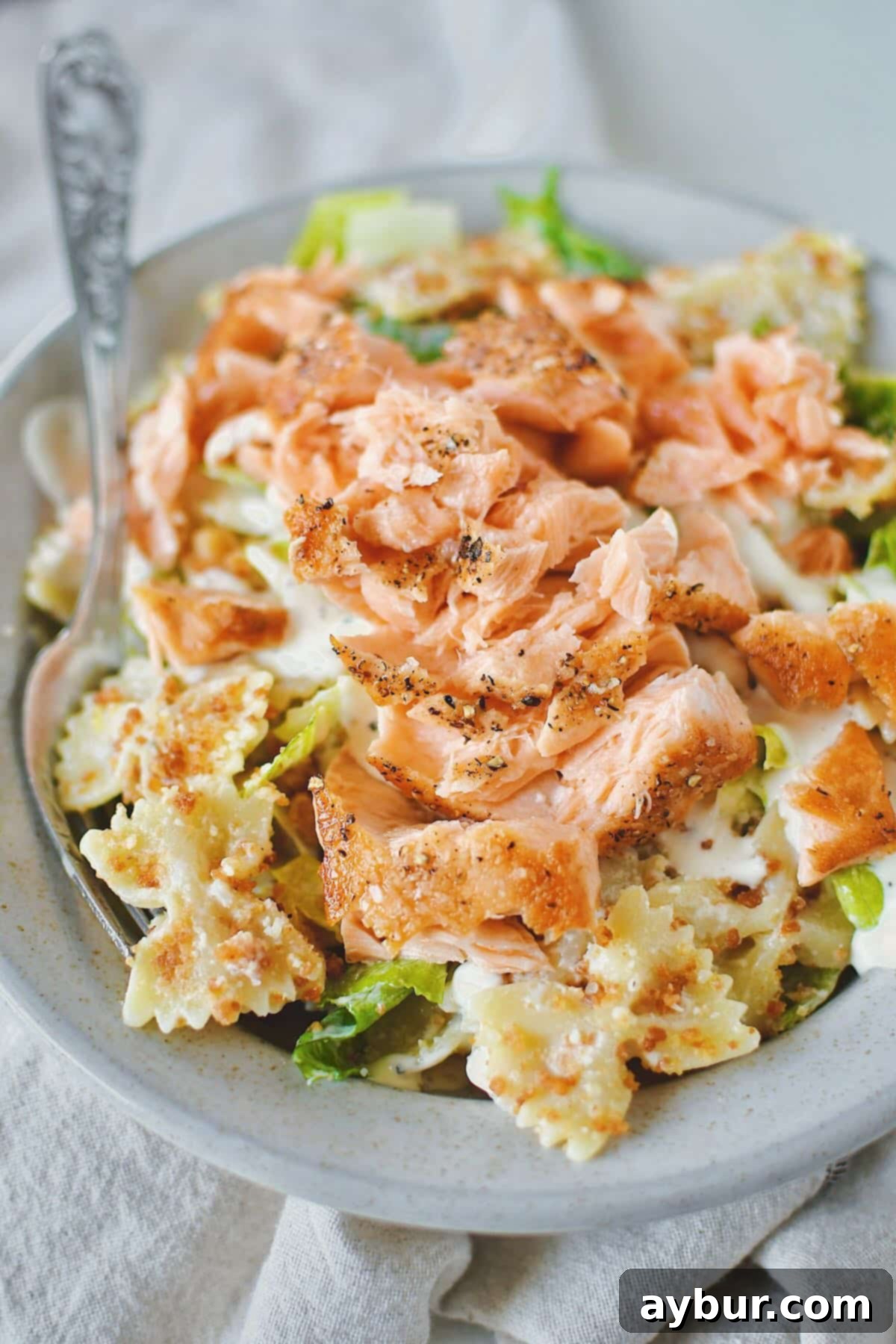 Caesar Pasta Salad served in a rustic bowl, generously topped with a perfectly pan-seared salmon fillet flaked over the top, creating a complete meal.