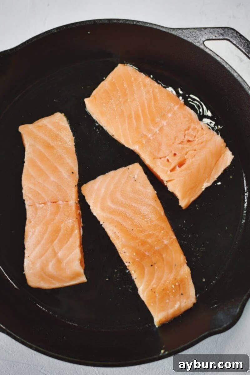 Raw salmon fillets, seasoned and placed skin-side down in a smoking hot cast iron pan with a touch of olive oil, ready for searing.